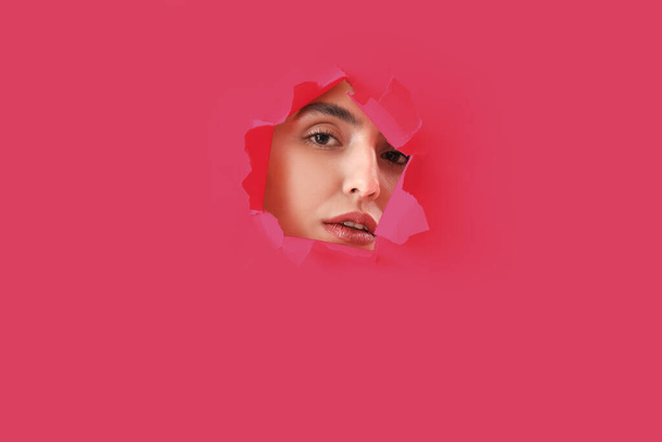 Giovane donna visibile attraverso il foro in carta rosa - Foto, immagini