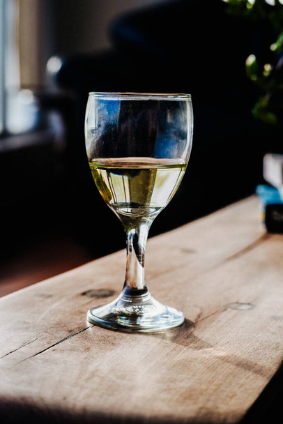 This stock photo showcases a glass of white wine on a wooden coffee table, perfect for any wine lover's collection. The clear glass allows the pale yellow color of the wine to shine through, making for an elegant and sophisticated image. The wooden t - Photo, Image