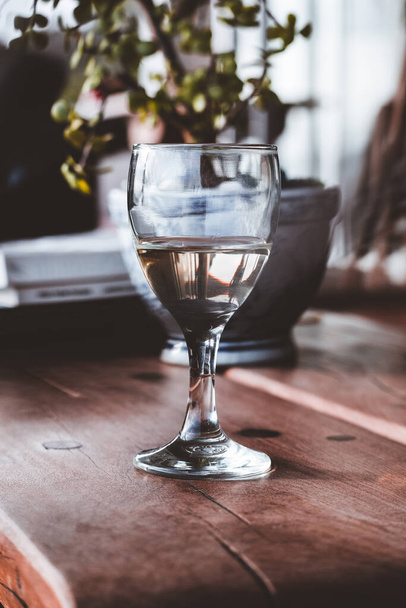 Αυτή η φωτογραφία αρχείου εμφανίζει ένα ποτήρι λευκό κρασί σε ένα ξύλινο τραπεζάκι του καφέ, ιδανικό για τη συλλογή κάθε λάτρη του κρασιού. Το διαυγές γυαλί επιτρέπει το απαλό κίτρινο χρώμα του κρασιού να λάμψει μέσα, κάνοντας για μια κομψή και εκλεπτυσμένη εικόνα - Φωτογραφία, εικόνα