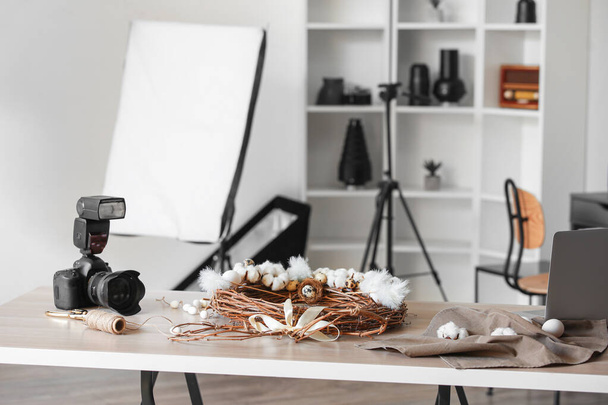 Câmera profissional e grinalda de Páscoa na mesa no estúdio de fotos - Foto, Imagem