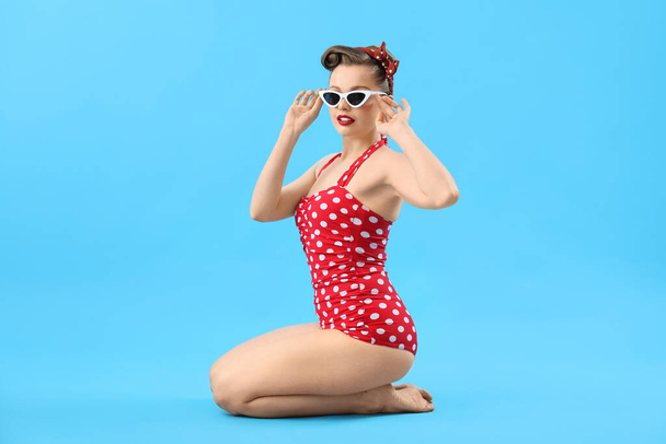 Young pin-up woman in polka dot swimsuit on blue background - Foto, afbeelding