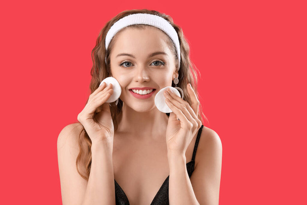 Young woman removing makeup with cotton pads on red background, closeup - Photo, image
