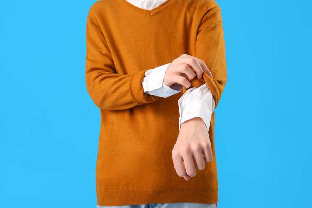 Teenage boy rolling up his sleeve on blue background, closeup - Foto, afbeelding