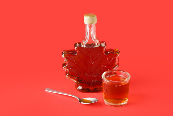 Bottle and glass of tasty maple syrup on red background - Photo, Image