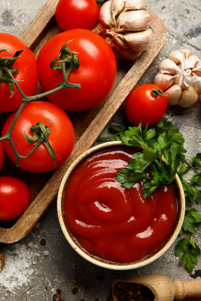 Bowl with tasty ketchup and fresh vegetables on grunge background - Fotó, kép