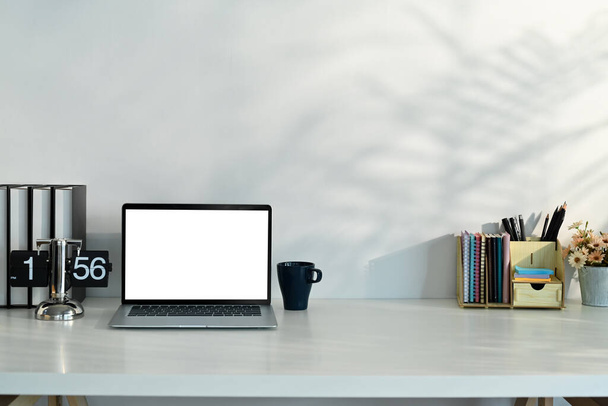 Kotitoimiston työpöytä kannettavalla tietokoneella, kirjat, kahvikuppi ja paperitavarat valkoisella pöydällä. - Valokuva, kuva