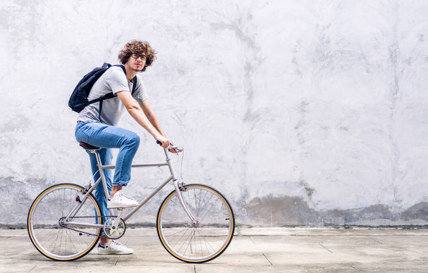 Portret niezobowiązującego hipstera przystojnego biznesmena z plecakiem patrzącego w kamerę podczas dojazdów do pracy na rowerze po ulicy droga do pracy. - Zdjęcie, obraz