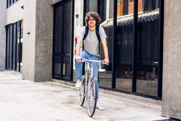 İş seyahati bisiklet konsepti, işe giderken bisiklet sürerken sırt çantasıyla kameraya bakan sıradan hippi yakışıklı işadamının portresi. - Fotoğraf, Görsel