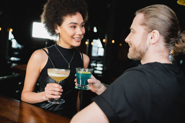 Smiling african amercan woman holding pisco sour cocktail near blurred friend in bar  - 写真・画像