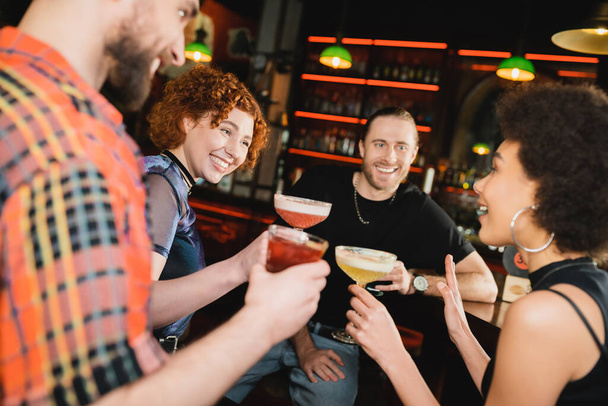 Cheerful people looking at african american friend with cocktail talking in bar  - Photo, Image