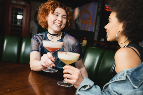 Sorridente interrazziale fidanzate holding blurred cocktails in bar  - Foto, immagini