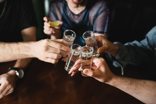 Ausgeschnittene Ansicht von interrassischen Freunden mit Tequila-Gläsern mit Salz in der Bar  - Foto, Bild