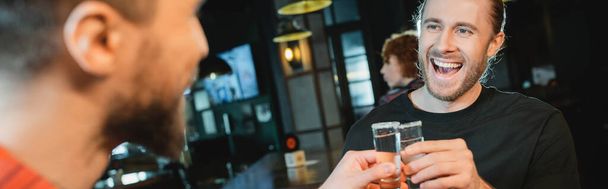Excited man clinking tequila with blurred friend in bar, banner  - Фото, зображення