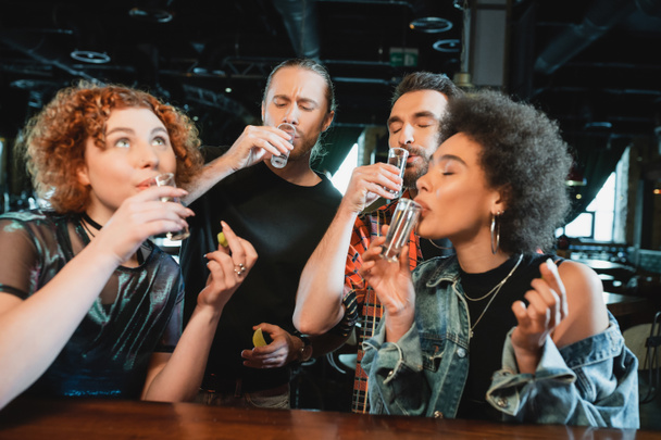 Amigos multiétnicos tomando tragos de tequila y sosteniendo lima fresca en el bar  - Foto, Imagen