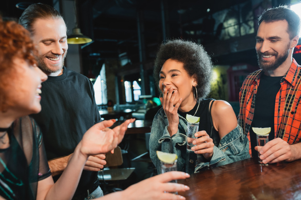 African american woman laughing near friends with tequila shots in bar  - Photo, Image