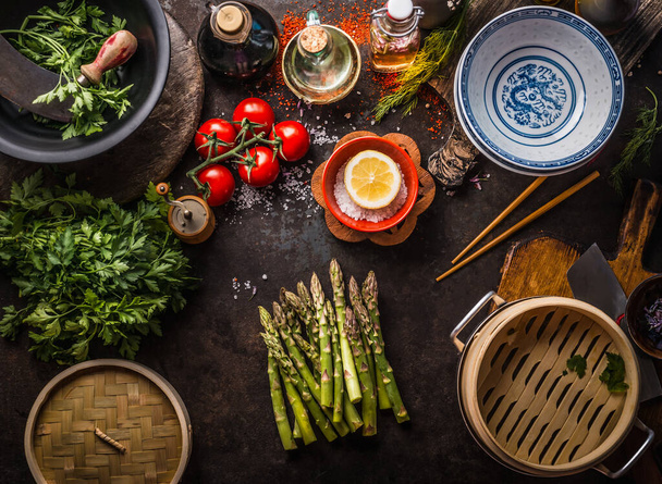 Green asparagus bunch , asian bamboo steamer and fresh tasty ingredients for healthy vegetarian eating and cooking in asian style on rustic table with chopsticks and empty bowls, top view - Photo, Image