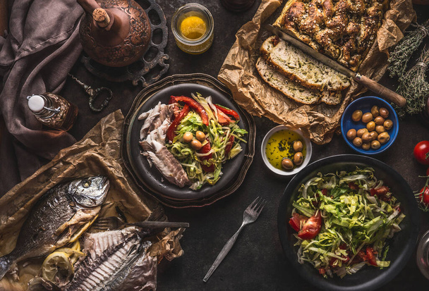 Salad bowl with backed fish and homemade bread on on dark rustic table, top view. Mediterranean lunch or dinner. Healthy food - Фото, зображення