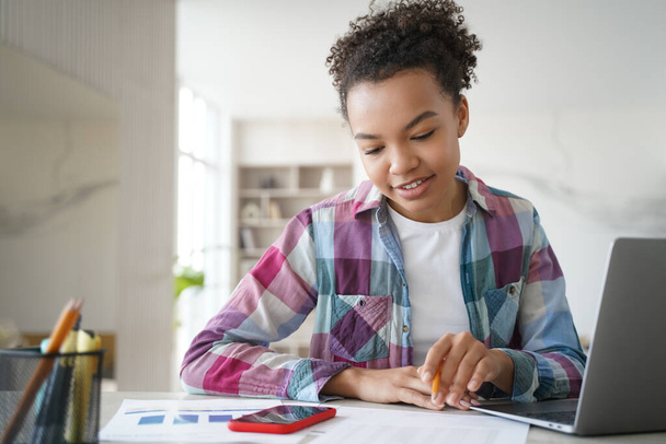 Jóképű afro iskolás lány távirányítót tanul otthon és házi feladatot csinál. A tinédzser lány az asztalnál ül a számítógép előtt, online vizsgázik. Távoli tanulás az iskolában vagy főiskolán zoom segítségével. - Fotó, kép
