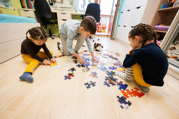 Children connecting jigsaw puzzle pieces in a kids room on floor at home.  Fun family activity leisure.  - 写真・画像