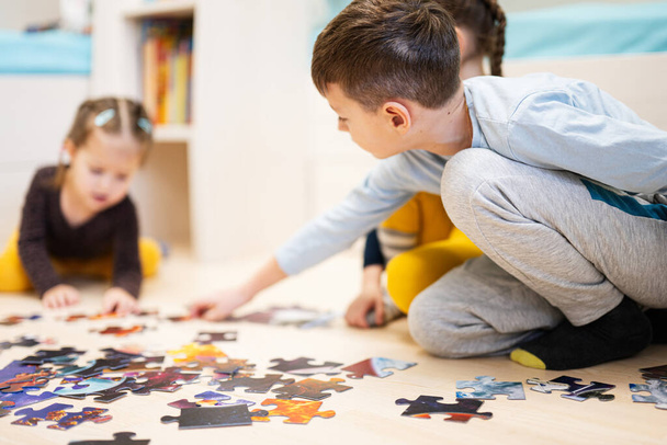 Children connecting jigsaw puzzle pieces in a kids room on floor at home.  Fun family activity leisure.  - Fotó, kép