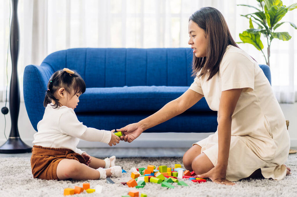 Портрет счастливой любви - семейная мама с маленькой девочкой, улыбающаяся, тренирующаяся в умении играть с игрушечными деревянными блоками настольная развивающая игра дома - Фото, изображение