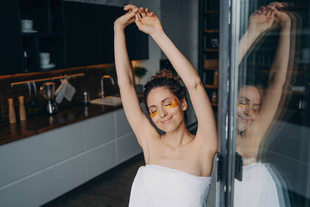 Freshness and relaxation. Pure skin after shower. Attractive young hispanic lady wrapped in towel after bathing enjoying evening at home or hotel room. Spa resort, daily care and beauty routine. - Photo, Image
