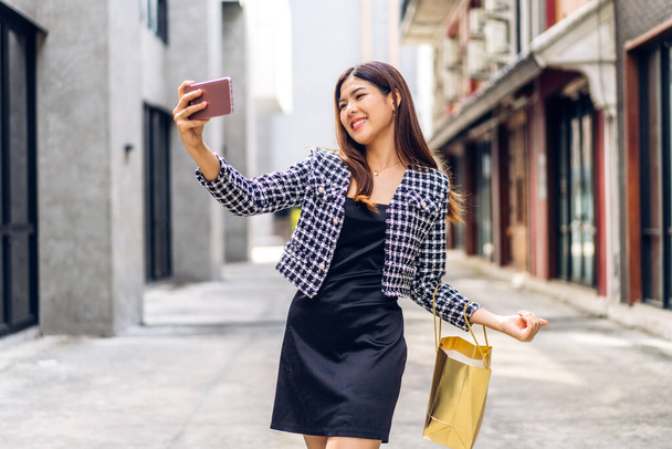 Portrait of smiling beauty asian fashion happy woman relax and enjoy shopping time summer sale walk and holding shopping colorful bag to buy something purchases use smartphone at store - Photo, Image