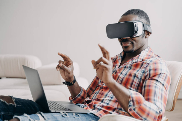 Afroamerikaner Softwaredelevoper mit Virtual-Reality-Brille arbeitet im Cyberspace am Laptop. Moderner schwarzer Programmierer, der freiberuflich VR-Spiele oder Anwendungen programmiert. - Foto, Bild