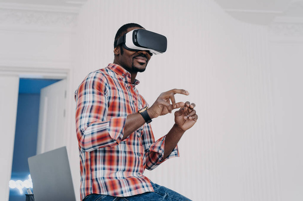 Modern african american man in VR glasses enjoy virtual tour in augmented cyberspace, touch 3d objects, interacting with digital interface. Black guy uses virtual reality goggles for online shopping. - Fotoğraf, Görsel