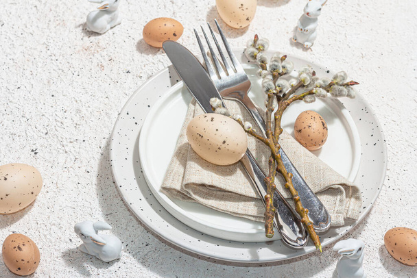 Easter table setting with eggs, rabbits and willow. Traditional festive symbols, greeting card, flat lay. Trendy hard light, dark shadow, plaster background, close up - Foto, imagen