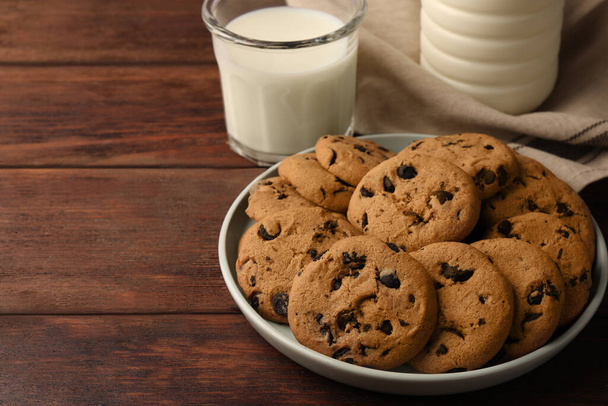 Delicious chocolate chip cookies and milk on wooden table. Space for text - Fotó, kép