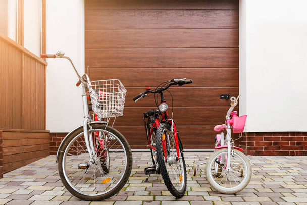 Family Bikes Riding concept. Children Bikes and Adult Bicycle under House Garage Door. Bicycles for Family Riding Together - Fotoğraf, Görsel