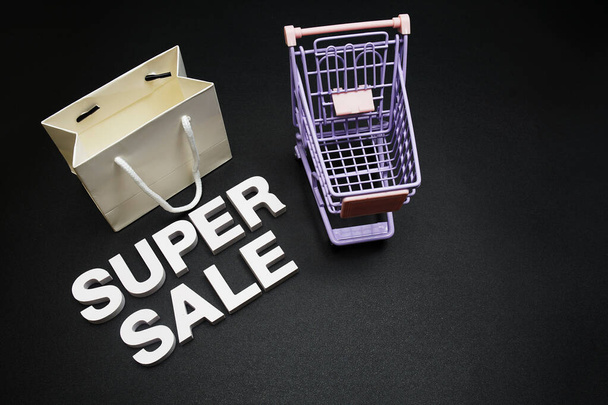 Super sale alphabet letters with alarm clock, shopping bag and trolley shopping cart on black background - Foto, Imagem