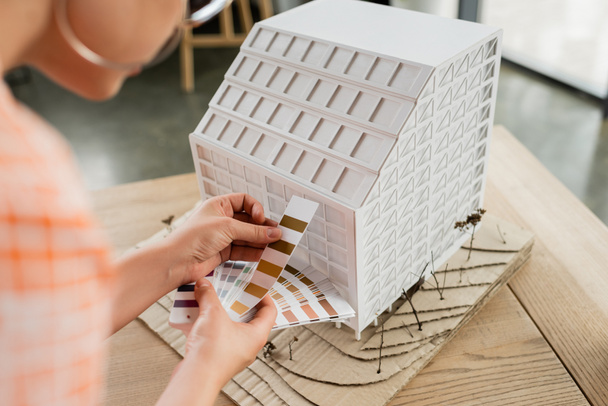 cropped view of architectural designer holding color palette near residential house model in office - 写真・画像