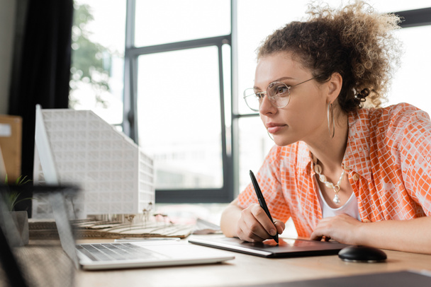 сфокусированный архитектурный дизайнер с помощью графического планшета и глядя на ноутбук во время работы в офисе  - Фото, изображение