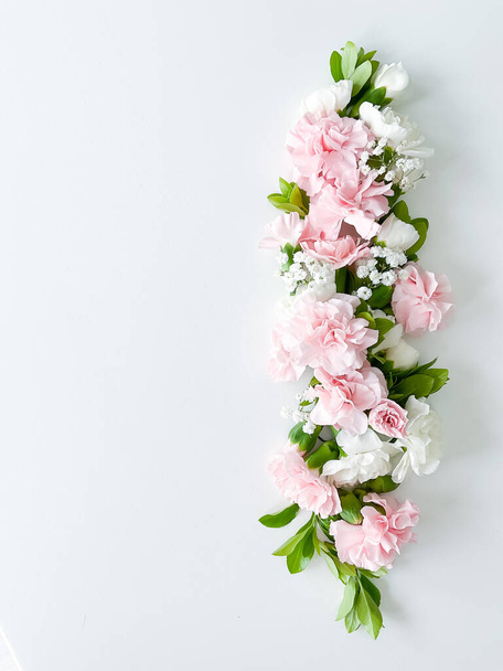 Beautiful delicate blooming floral frame of pink carnations, gypsophila, buds, leaves on a white background, top view, flat lay - Fotó, kép
