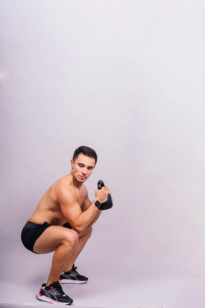 Strong young muscular focused fit man with a big muscles holding heavy kettlebells - Photo, Image