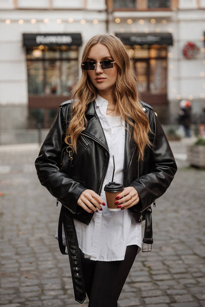 Fashionable  blonde woman model with  black leather jacket and style sunglasses walking the city street - Foto, afbeelding