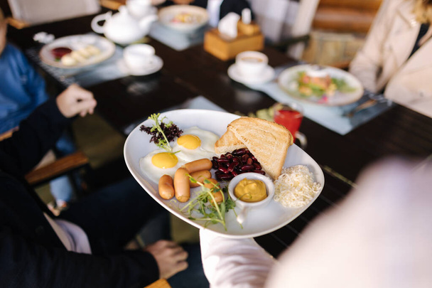 The waitress brings food for customers. English breakfast, eggs, sausages, red beans, toasted bread and butter on plate. High quality photo - Фото, зображення