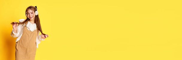 Emoções alegres. Bandeira de jovem alegre com cabelo comprido usando fones de ouvido e sorrindo sobre fundo amarelo. Conceito de emoções humanas, vida estudantil, moda, primavera, verão, saúde mental - Foto, Imagem