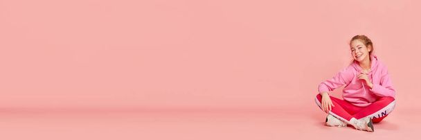 Emoções alegres. Bandeira de menina alegre vestindo roupas esportivas e sorrindo sobre fundo rosa. Conceito de esporte, emoções humanas, vida estudantil, primavera, verão, saúde mental, tempo de lazer - Foto, Imagem