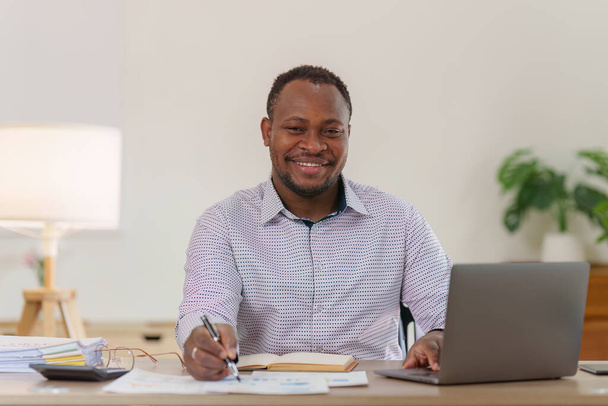 Glimlachende Amerikaanse Afrikaanse Banker of Accountant maakt financieel verslag en bestudeert jaarcijfers, analyseert winsten. Status van de boekhoudkundige controles van de financiële middelen. - Foto, afbeelding