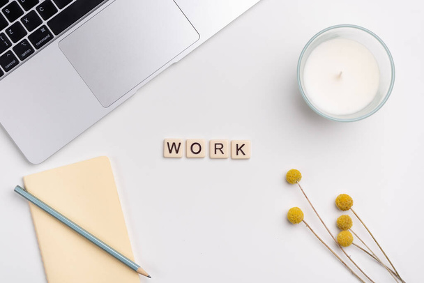 Clean workspace with laptop, pencil and notebook, candle and flowers on white background. The word WORK written with tile letters. Flat lay - Foto, imagen