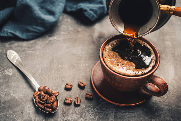 Verser une boisson au café noir de la cafetière turque jezve dans une tasse d'argile sur fond sombre. - Photo, image