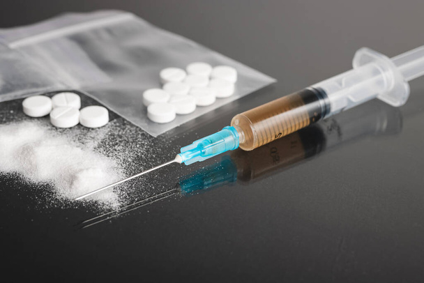 Kemény illegális drogok sötét háttérrel, kokain vagy heroin fehér por, fehér tabletták és fecskendő egy adag. A kábítószerrel való visszaélés és a függőség fogalma. - Fotó, kép