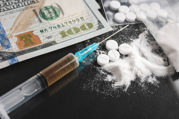 Drugs op donkere achtergrond, cocaïne of heroïne wit poeder, witte pillen, spuit met een dosis en ons dollargeld. Drugsmisbruik en verslaving. - Foto, afbeelding