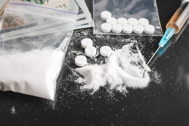 Drugs on dark background, cocaine or heroin white powder, white pills, syringe with a dose and us dollar cash. Drug abuse and addiction concept. - Photo, Image