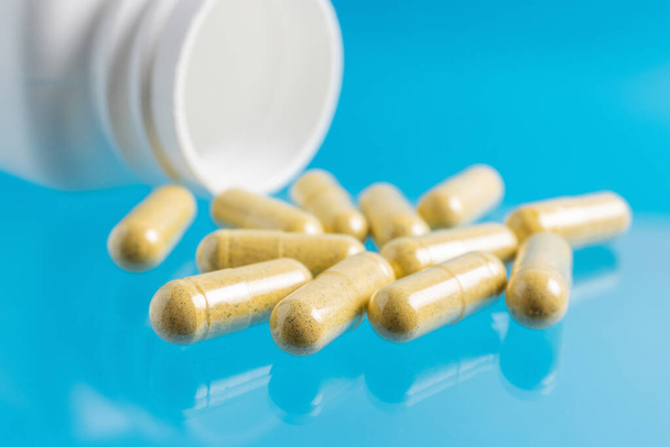 Желтые куркумы терапевтические капсулы, травяные витамины таблетки или лекарства для лечения на голубом фоне, медицина и здравоохранение концепции, крупным планом. - Фото, изображение