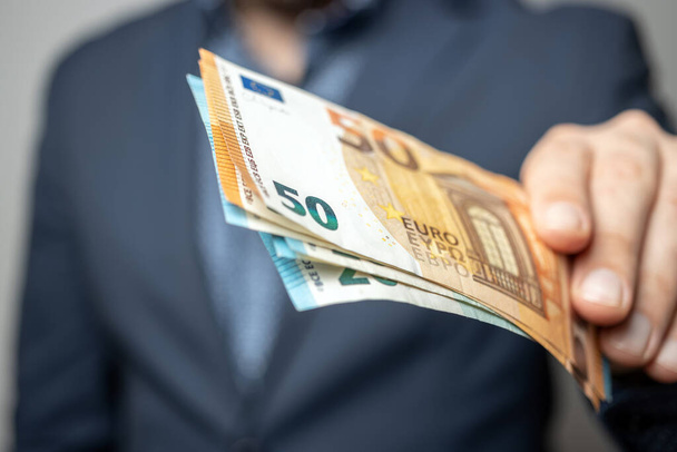 Well dressed man holding in the hand or giving bunch of money, euro banknotes, European Union paper currency. - Photo, Image