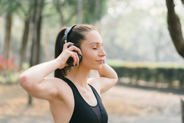 A relaxed woman is shown enjoying music while jogging through a public park. The young lady is feeling free, relaxed, and happy - Photo, image